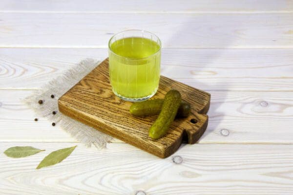 A glass of green juice and Dr. Dill's Real Pickle Juice on a wooden cutting board.
