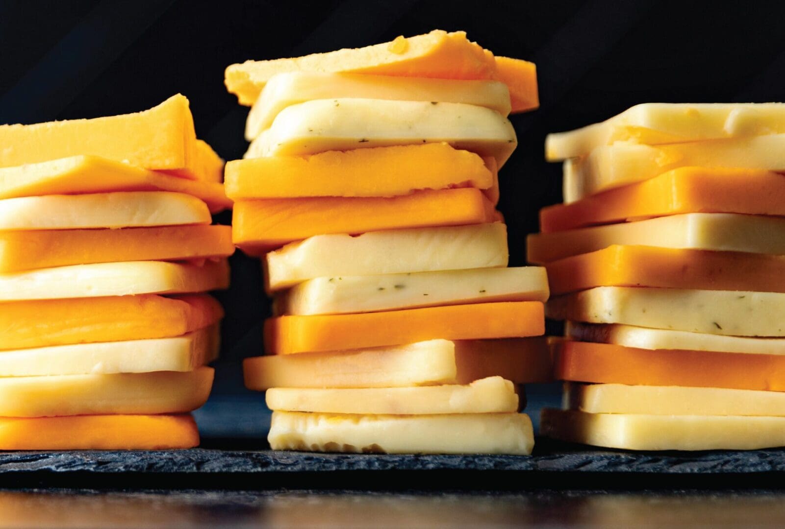 A stack of specialty cheese slices on a black background.